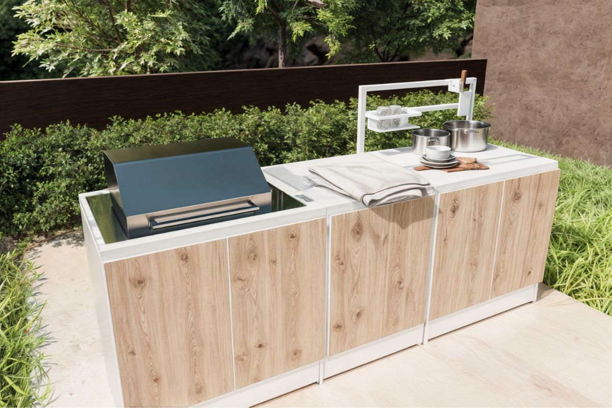 Prime outdoor kitchen with three workbench modules, integrated BeefEater barbecue, Top Structure for hanging utensils, white marble-effect countertop, and wood-look cabinet fronts
